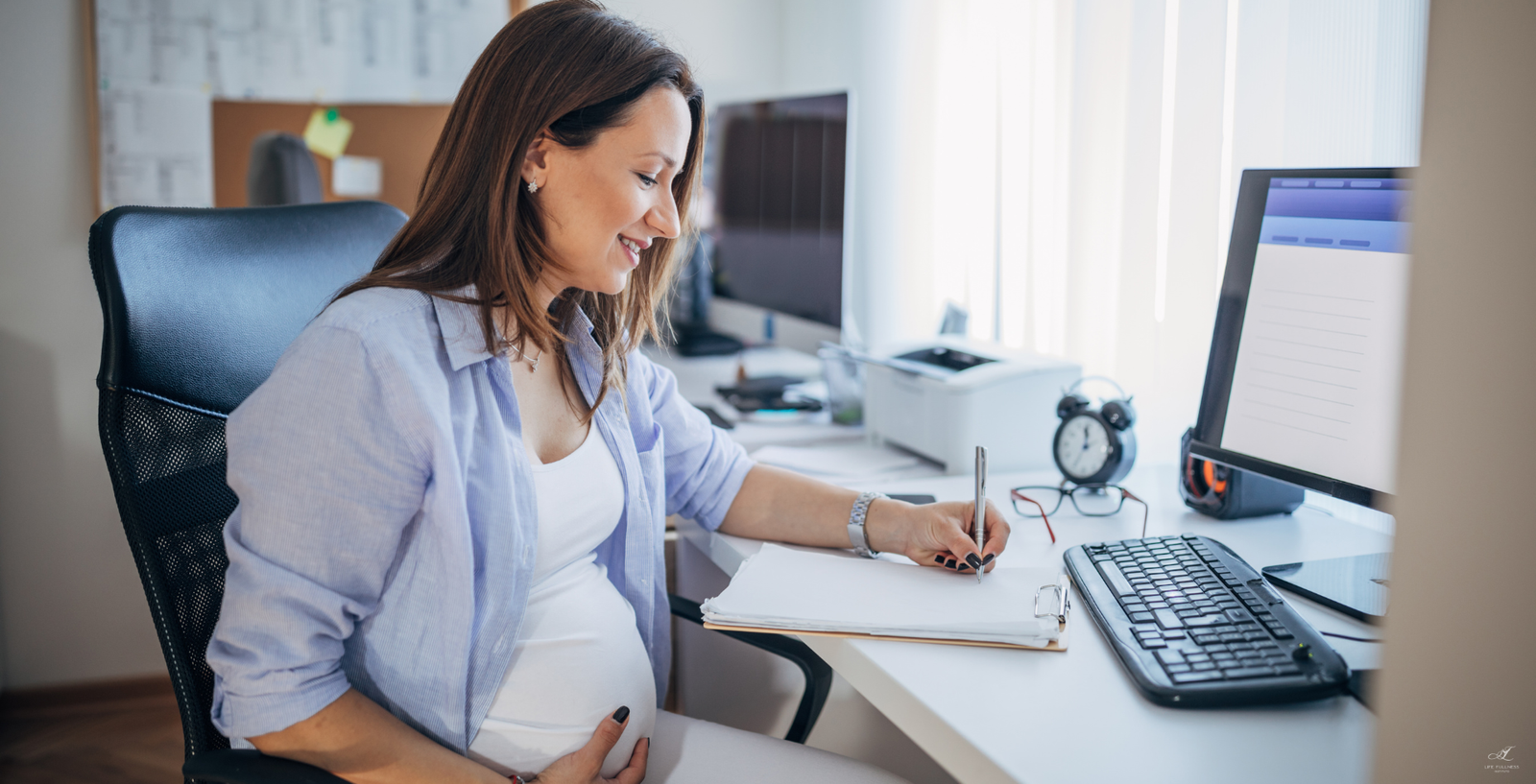 mulher grávida na frente do computador. Uma das mãos na barriga e outra anotando em um papel.